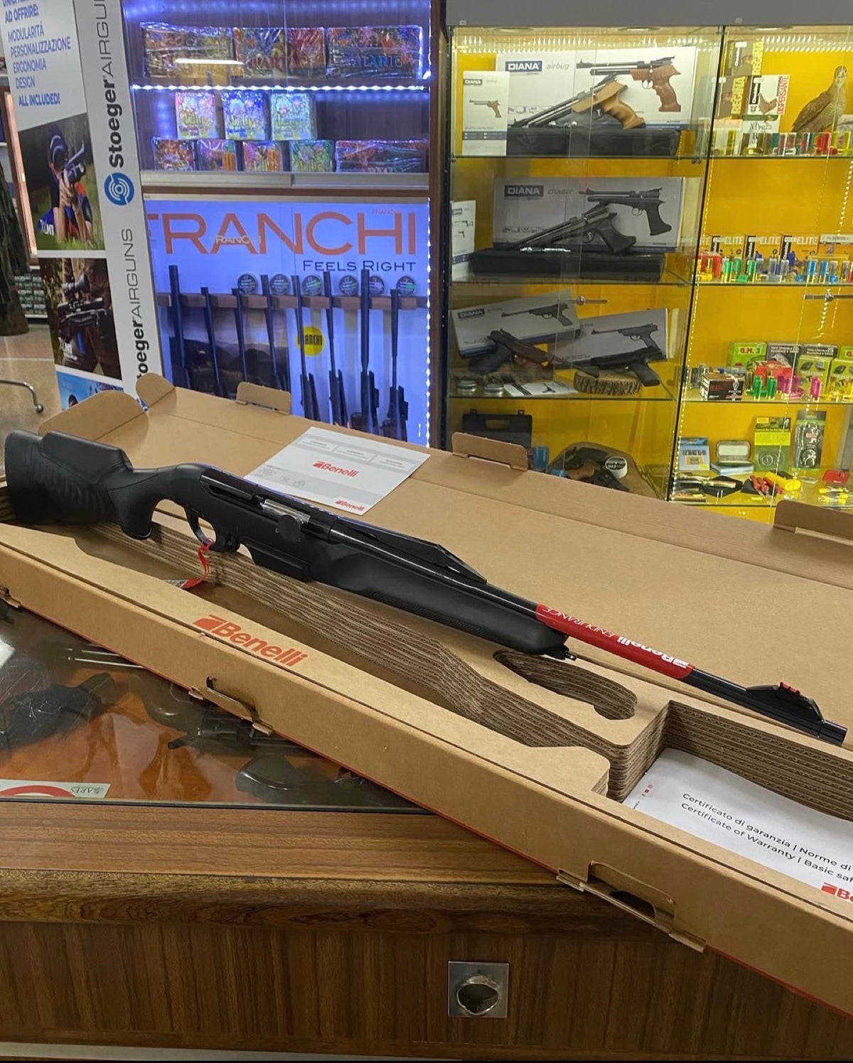 Carabina Benelli Endurance nella confezione sul banco del reparto armeria, con la vetrina delle carabine ad aria compressa alle spalle